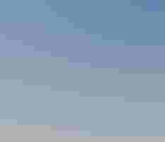 a person stands on a beach and looks through a spotting scope, facing left. In the background is the ocean and a blue sky with sparse clouds.